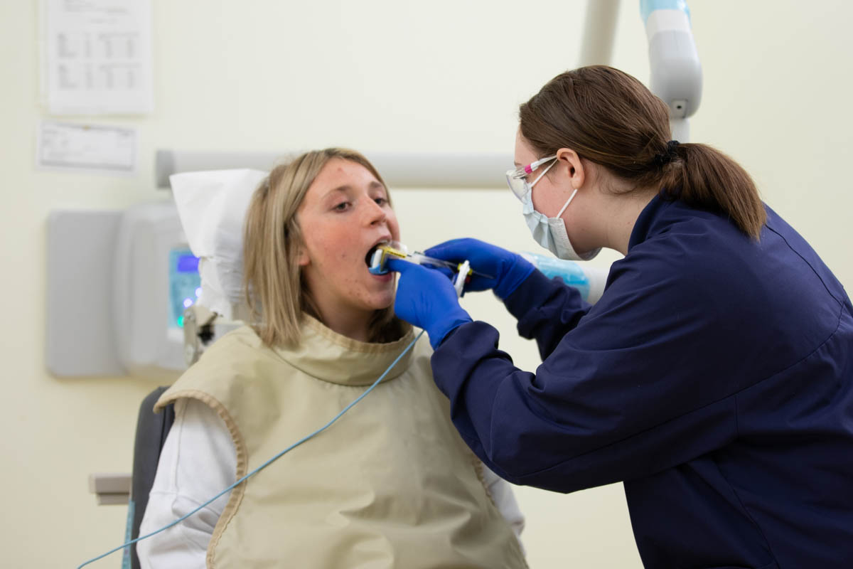 Female dental assistant taking mouth x-rays of woman